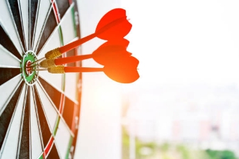 Drei rote Dartpfeile stecken im Bulls-Eye